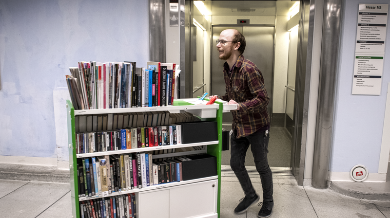 Man med bokvagn från patientbiblioteket kliver ur en hiss på USÖ